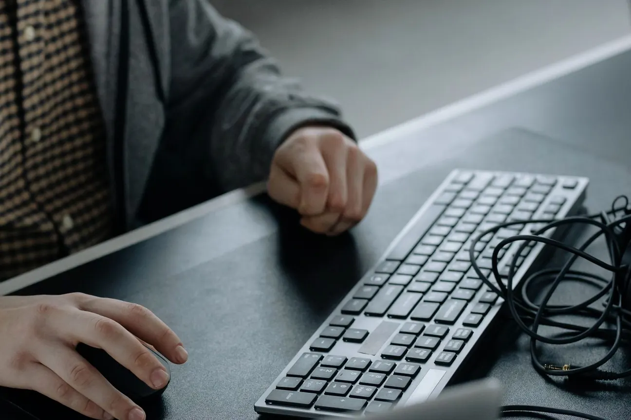 Hände an Maus und Tastatur an einem dunklen Schreibtisch